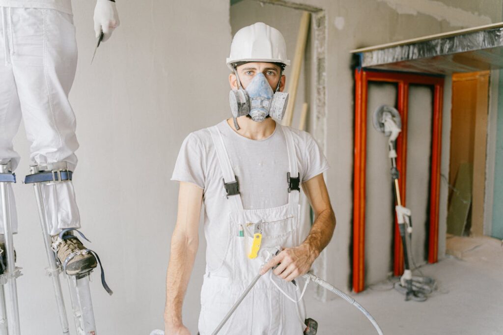 A construction worker wearing protective gear and prepping the wall during renovation indoors.