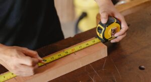 Close-up of a carpenter measuring a wooden plank with a tape measure on a workbench.