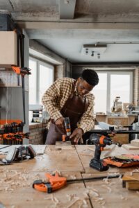 African American man drilling wood in a bright workshop, focused on carpentry task.