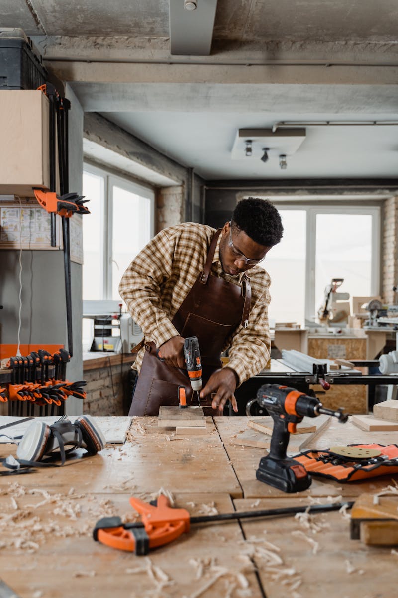 African American man drilling wood in a bright workshop, focused on carpentry task.