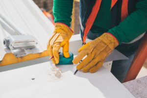 Electrician measuring on rooftop, wearing protective gloves, during daylight.
