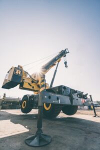 A powerful crane with industrial lifting equipment at a construction site under a clear blue sky.